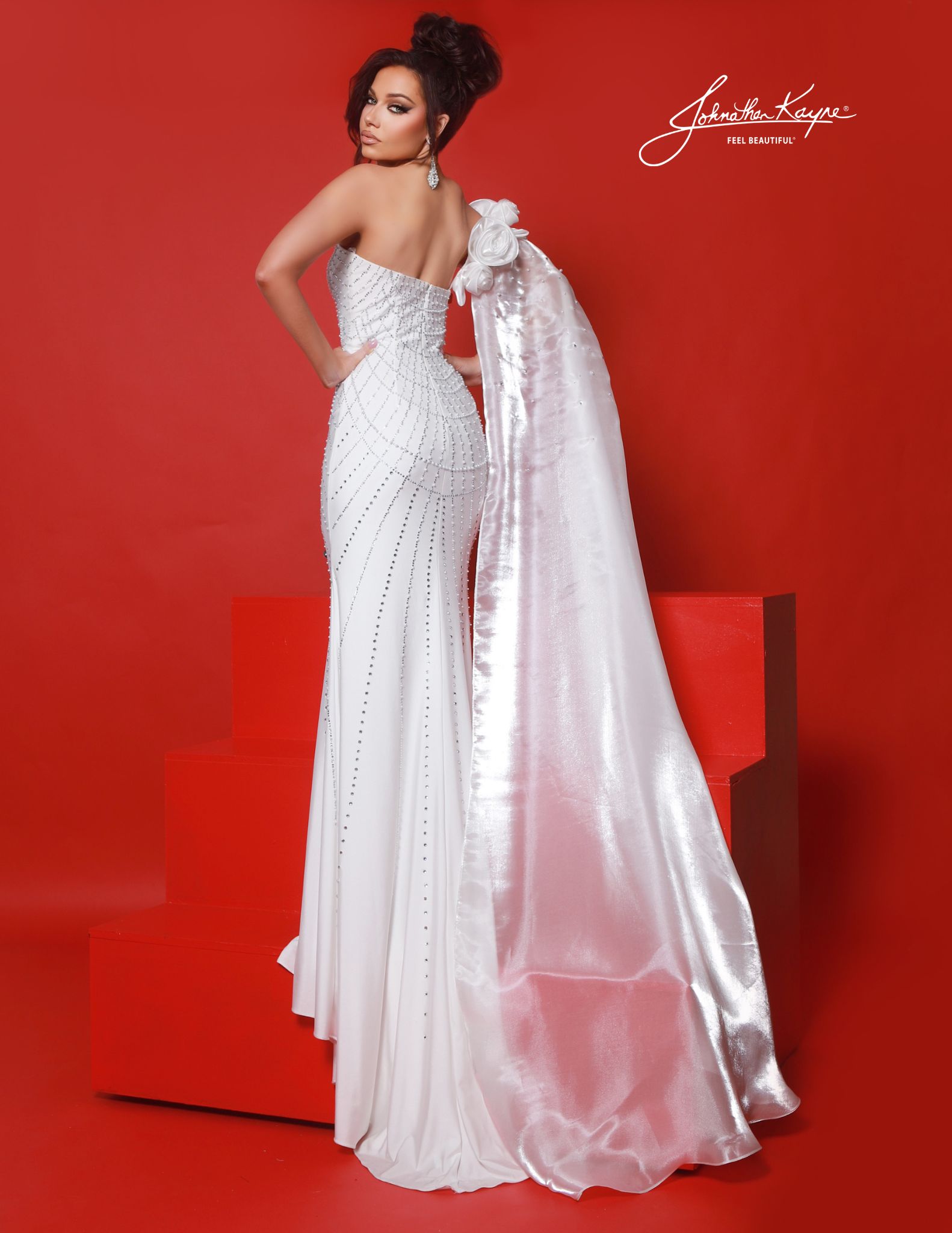 Back view of white embellished pageant gown with cape, pearl-studded back design and train detail, showing full-length cape perfect for red carpet and grand entrances.